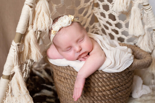 a beautiful baby sleeps in a wicker basket that stands in a wicker tent. beige background with space for text with baby sleeping in a wicker basket. close-up portrait