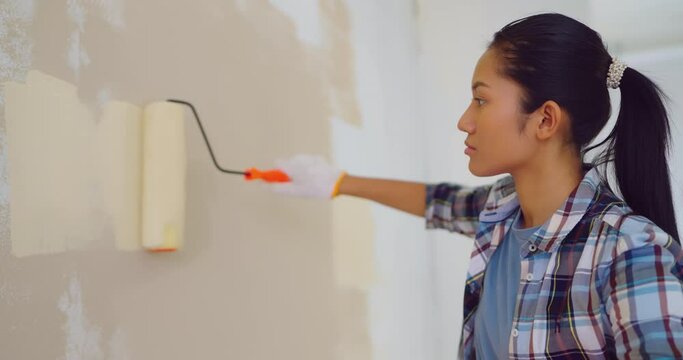 Beautiful asian woman paint wall in apartment. She painting walls with roller. Slow motion shot.