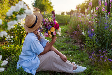 Woman gardener enjoying summer garden at sunset holding fresh roses. Farmer picked bouquet of...