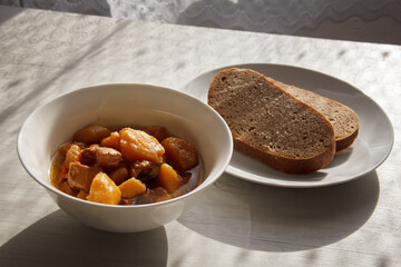 plate with stewed potatoes and meat on a wooden table and next to on a plate of bread. selective focus 