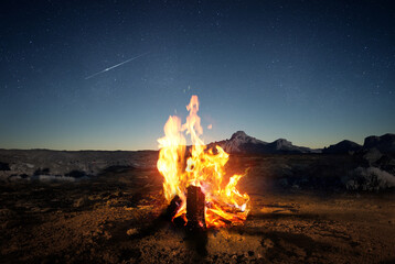 Exploring the wilderness in summer. A glowing camp fire at dusk providing comfort and light to...