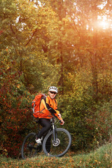 Fototapeta premium Candid outdoor shot of concentrated young rider in protective gear and track suit sitting on his bike in the depth of the forest. He is stuck to healthy lifestyle.