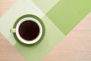 Green cup of coffee on the background of the pink wood table and tablecloth. View from top