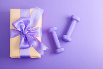 Holiday birthday party sport flat lay composition with purple dumbbells and craft gift with lilac bow on  violet paper background. Top view, horizontal orientation