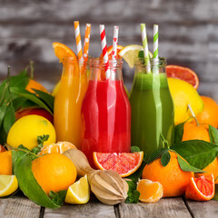 Fresh orange, blood orange juice and homemade lemonade in small bottles on old wooden table. Copy space background.