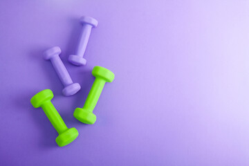Sport flat lay composition with purple and green dumbbells on violet concrete background. Top view,  horizontal orientation - obrazy, fototapety, plakaty