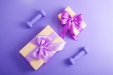 Holiday birthday party sport flat lay composition with purple dumbbells and craft gifts with lilac bow on  violet paper background. Top view, horizontal orientation