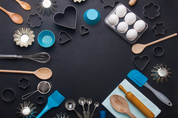 Baking background with eggs and kitchen tools: rolling pin, wooden spoons, whisk, sieve,  bakeware and shape cookie cutter on dark wooden background. Horizontal orientation with  copyspace, top view.