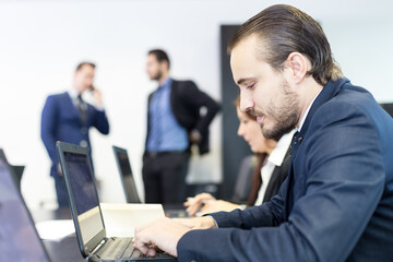 Workplace in modern corporate office with business people brainstorming. Businessman working on laptop during the meeting.