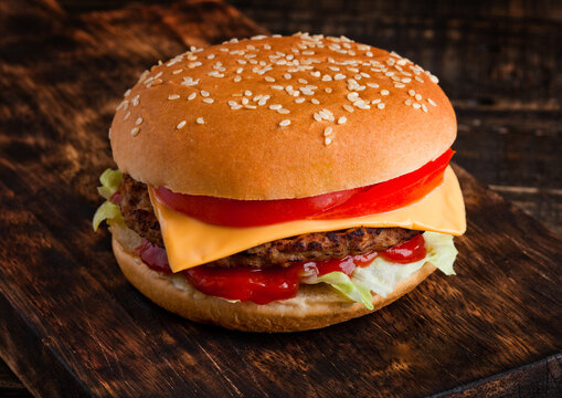 Classic beef cheeseburger with vegetables and sauce on wooden board background
