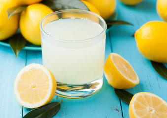 Glass of organic fresh lemon juice with raw lemons on blue wooden background - Powered by Adobe