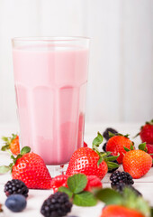 Milkshake glass with fresh summer berries smoothie on wooden background.Strwberries and raspberies with blueberries and blackberries.