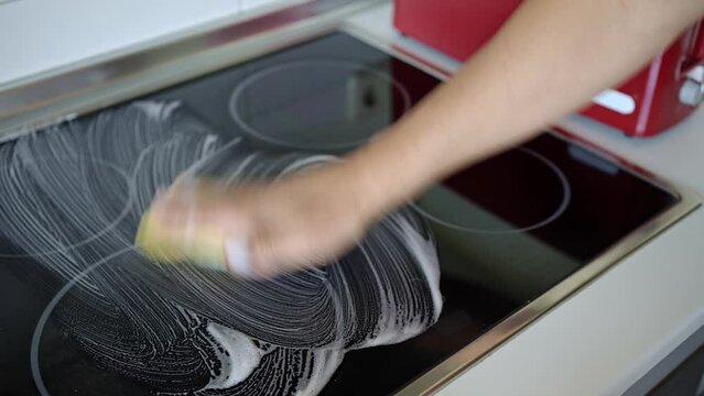 Soaping the glass ceramic for cleaning. Video of the hand of an unrecognizable person doing housework applying cleaning products with a scouring pad to the glass of the glass ceramic hob.