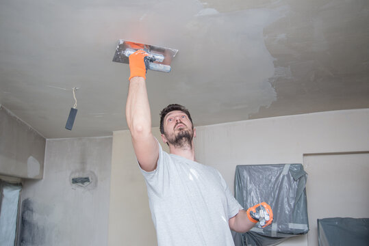 A worker with protective gloves is plastering the ceiling.