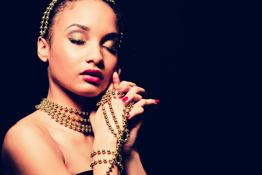Upscale Indian woman wearing gold jewellery and red lipstick on dark background