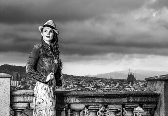Perfect evening with stunning view. trendy woman in long dress and straw hat against city panorama of Barcelona, Spain looking into the distance