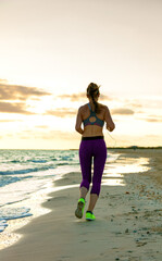 Refreshing wild sea side workout. Full length portrait of young woman in sport clothes on the seashore at sunset jogging