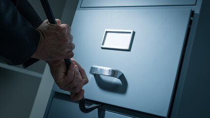 Burglar opening a drawer in the office at night using a crowbar, he is stealing confidential data...