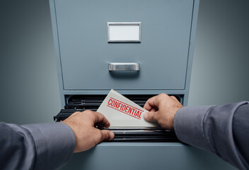 Office clerk searching for files in the filing cabinet, he finds a folder with confidential...