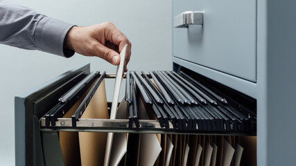 Office clerk searching for files into a filing cabinet drawer close up, business administration and...