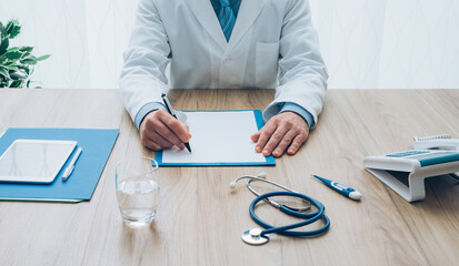 Professional doctor in his office working at desk and writing a medical report, healthcare and...