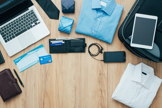 Businessman getting ready to leave for a business trip and packing a bag with formal clothing, accessories, laptop and plane tickets, traveling and business concept, flat lay