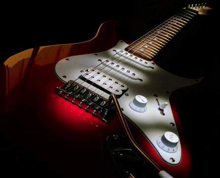 Six-string red electric guitar on a black background.