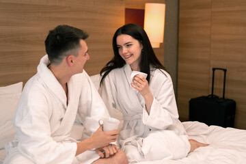 Obraz na płótnie Canvas young couple on honeymoon in hotel room having breakfast in room drinking coffee happy lovers travel concept