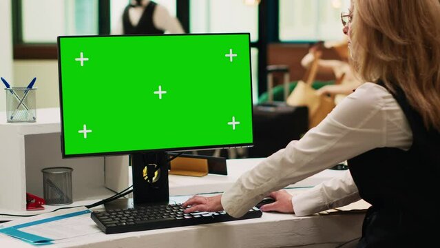Front desk staff using greenscreen on pc in resort lobby, checking chroma key display with isolated template. Hotel receptionist looking at blank copyspace on computer. Tripod shot.