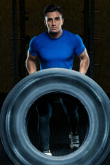 Fototapeta na wymiar portrait of a strong athlete with a large heavy wheel in the gym