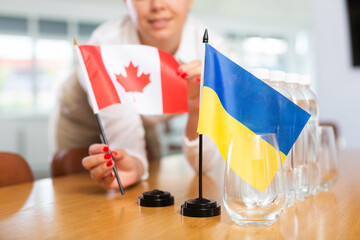 Preparation for international negotiations. Female office coordinator setting national flags of...