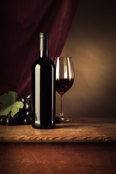 Red wine bottle and glass on a rustic wooden table, red cloth on background, wine tasting still life