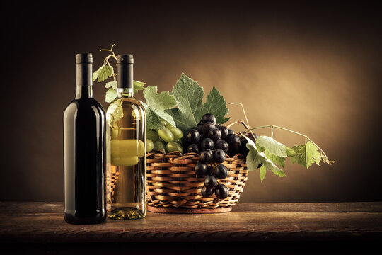 Wine bottles, grapes and vine leaves in a basket on a rustic wooden table, still life