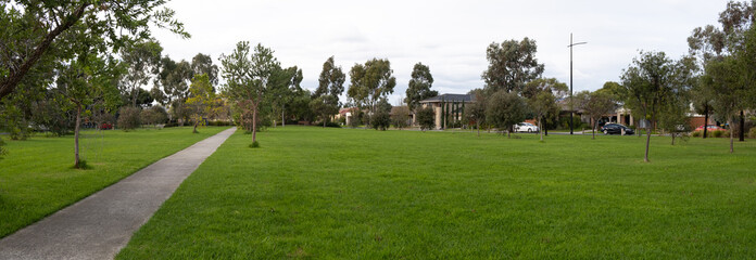 Panoramic view of a large green lawn in an suburban public park with some Australian houses in the...