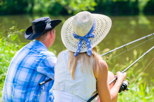 Couple, woman and man, sitting at river side with fishing rods angling for sport
