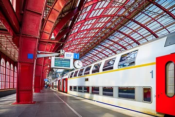 Photo sur Plexiglas Anvers Antwerp, Belgium. Central indoor railway station. Platform made of red metal constructions with clock and panel with departure or arrival schedule. Modern double decker high-speed train