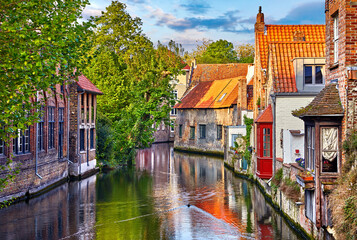 Obraz premium Bruges, Belgium. Medieval ancient houses made of old bricks at water channel with boats in old town. Summer sunset with sunshine and green trees. Picturesque landscape.