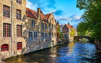 Fototapeta na wymiar Bruges Belgium vintage stone houses and bridge over canal ancient medieval street picturesque landscape in summery sunny day with blue sky white clouds.