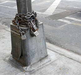 Heavy metal chains and padlocks wound around the base of a streetlight at the edge of a sidewalk