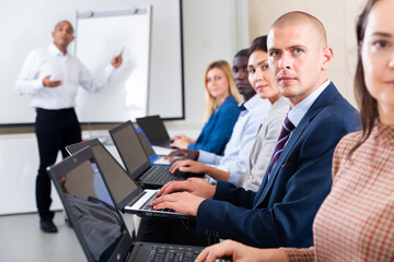 Side view of concentrated businessman working on laptop with group of colleagues during corporate seminar