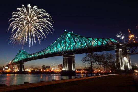 Fireworks explode over bridge, reflection in water. Montreal’s 375th anniversary. luminous colorful interactive Jacques Cartier Bridge. Bridge panoramic colorful silhouette by night.