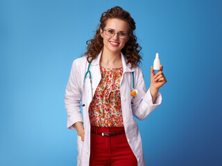 smiling pediatrist woman in white medical robe showing nasal drops isolated on blue background