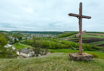 Fototapeta na wymiar Wooden christianity religious cross near Rukomysh Cave temple and spring country fields and village, Buchach District, Ternopil Region, Ukraine.