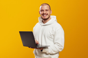 Successful caucasian young man student freelancer using laptop, watching webinars, working remotely, e-learning online isolated over yellow background