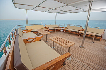 Obraz premium Rear teak deck of a large luxury motor yacht with chairs sofa table and tropical sea view background