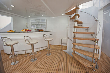 Wooden curved spiral staircase and bar area on sundeck of large luxury motor yacht