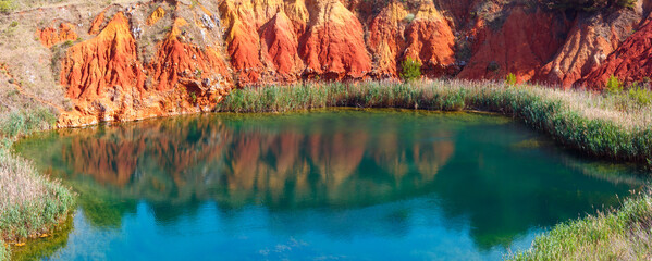 The lake in old bauxite's red soils quarry cave in Apulia, Otranto, Salento, Italy. The digging was filled with natural waters. Two shots stitch high-resolution panorama.