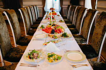 Long served table with plates, glasses, napkins, chairs and dishes