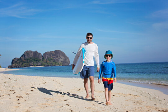 happy family of two, father and son, walking at the beach holding surf board, adventure vacation concept
