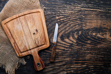 old cutting board with knife on dark wooden table. View from above. copyspace.